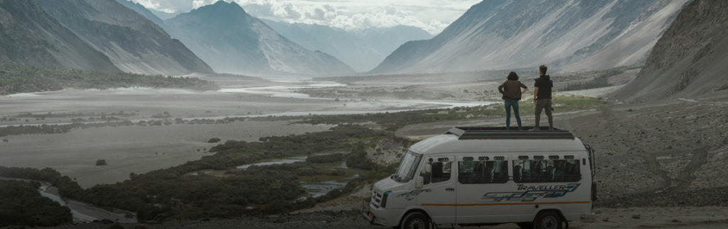 Une femme et un homme sont debout sur un van et regardent à l'horizon. Paysage montagneux.