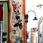 Photo d'une rue bruxelloise. Un pan de bâtiment est animé par des personnages de bande-dessinée