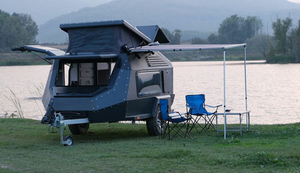 Photo de la caravane off road XP-3 de Camper X avec ses tables extérieures. Elle est posée sur un terrain.